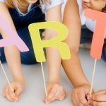 Children playing with colorful paper cutouts spelling 'ART' indoors.